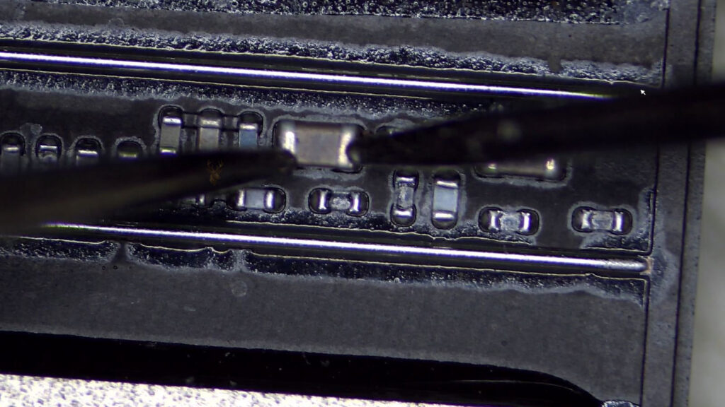 Computer circuit board being measured at an SMD capacitor to check for a short.