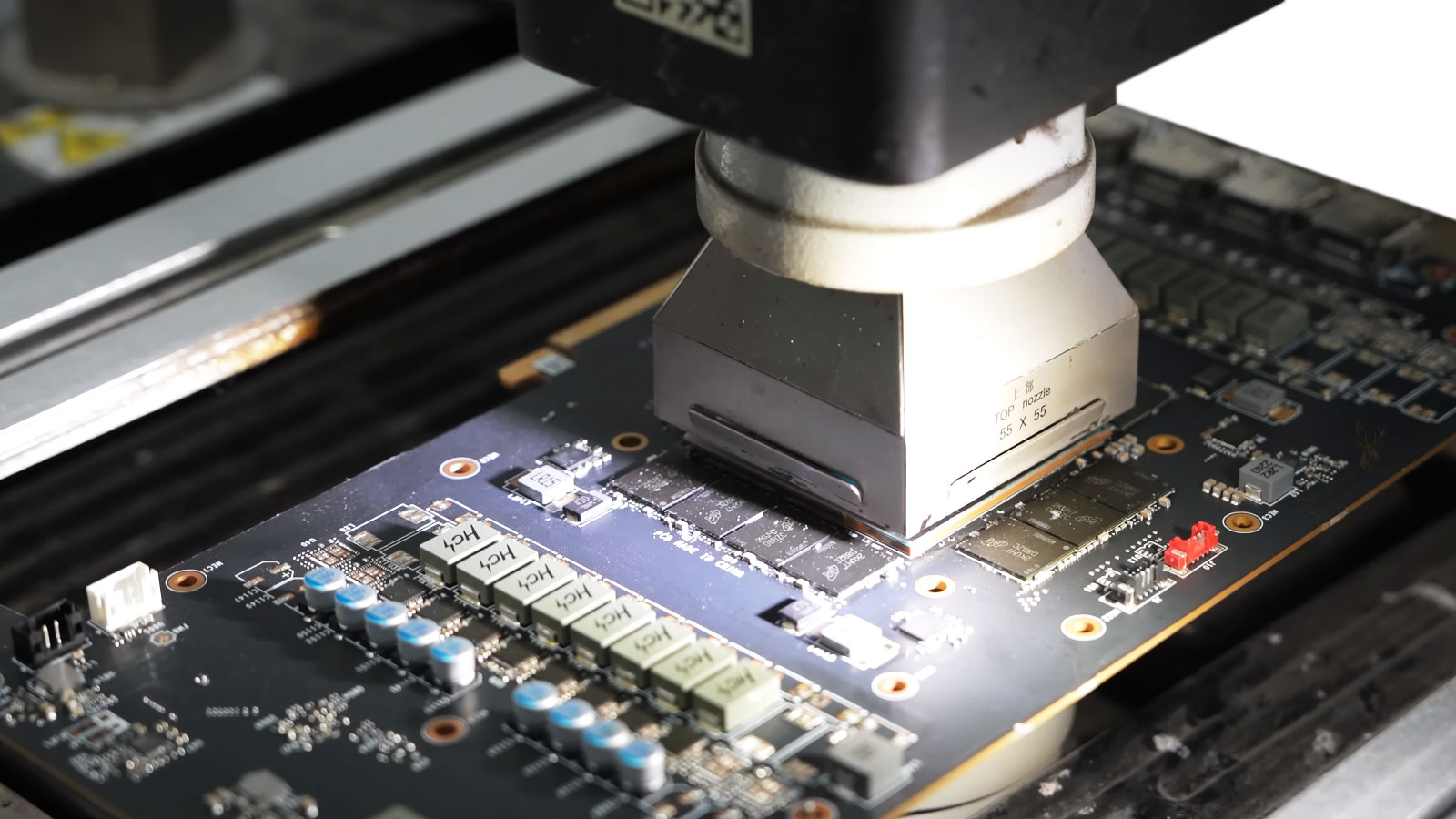 Reflow machine nozzle positioned over a video chip on a graphics card for removal and replacement.