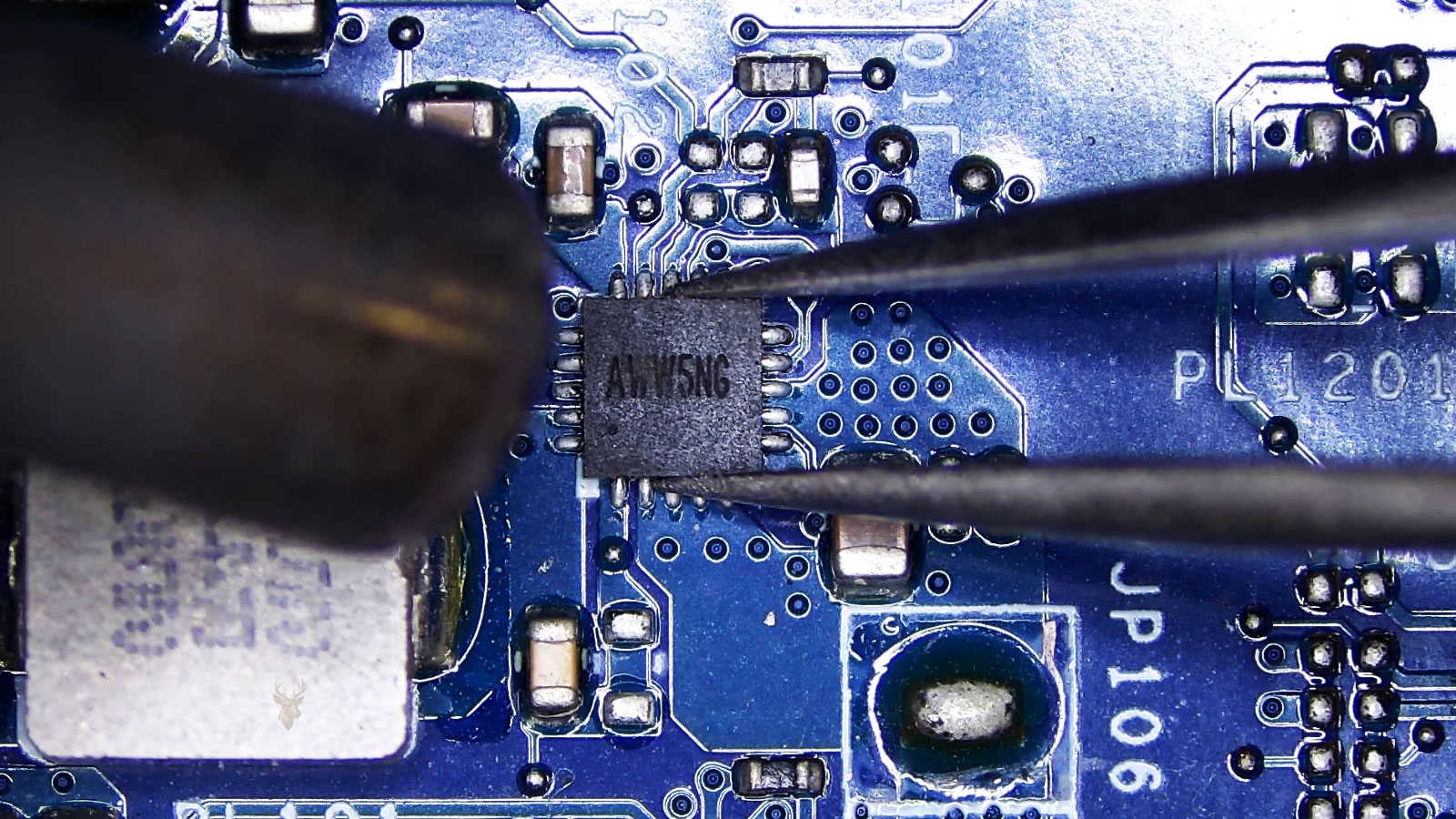 Close-up of a computer circuit board with an AWW5NG IC controller held by tweezers while a hot air nozzle points toward it.