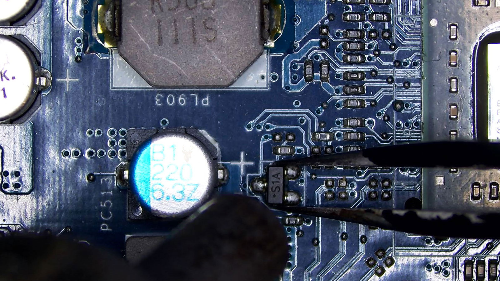 Technician removing a small SMD component labeled S1A from a computer board using tweezers and hot air rework.