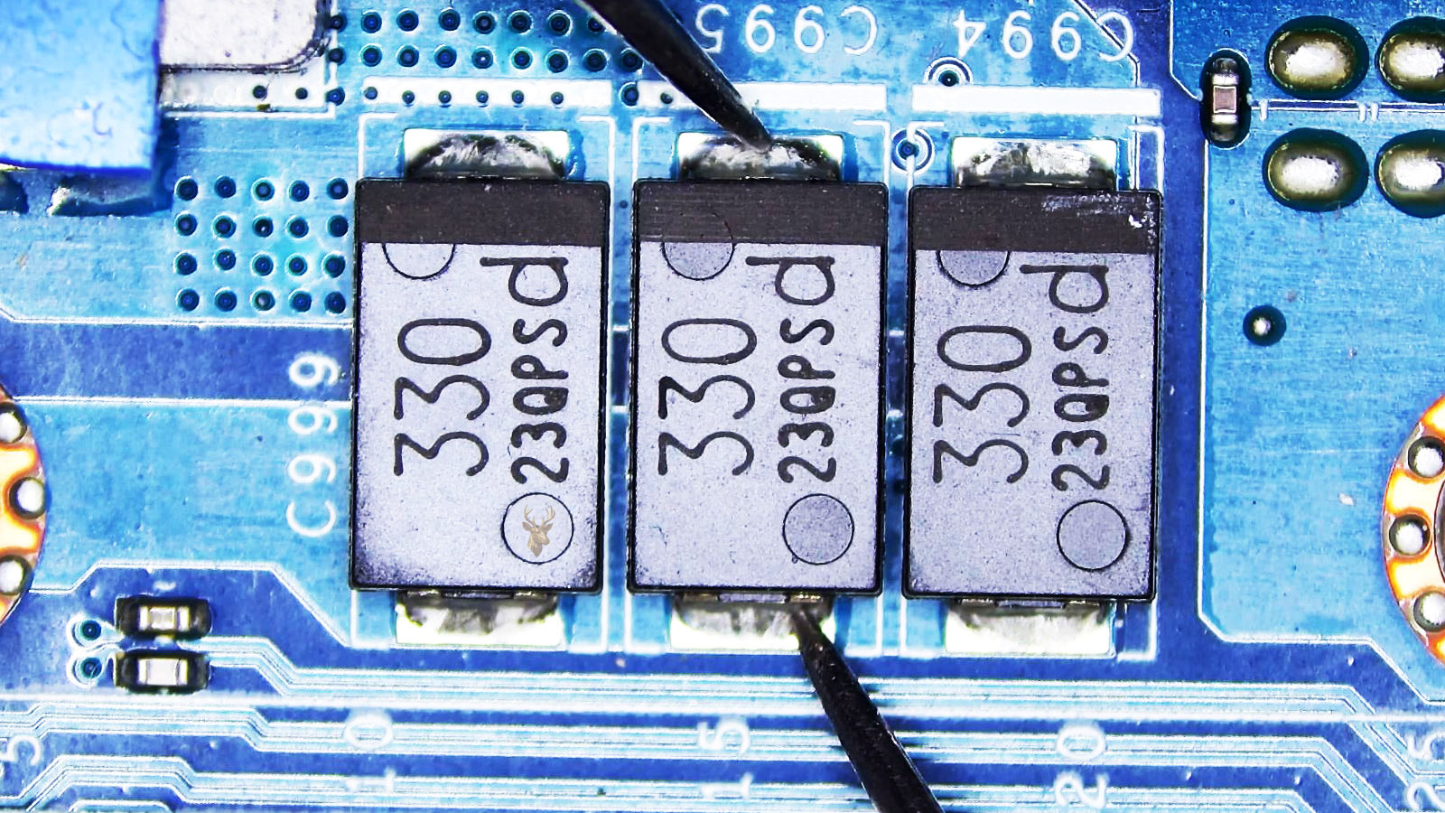 Close-up of a computer circuit board with three large 330 capacitors, including capacitor C995 being measured at the center.