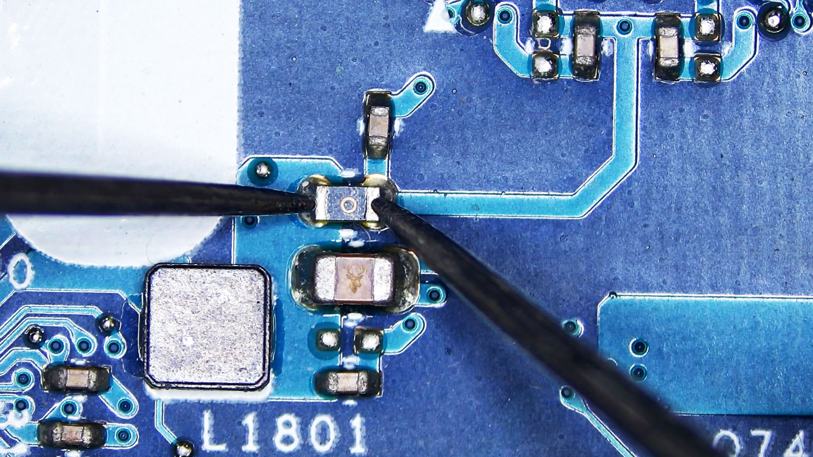 Close-up of a circuit board with capacitors, coils, resistors, and a fuse being tested with a multimeter.