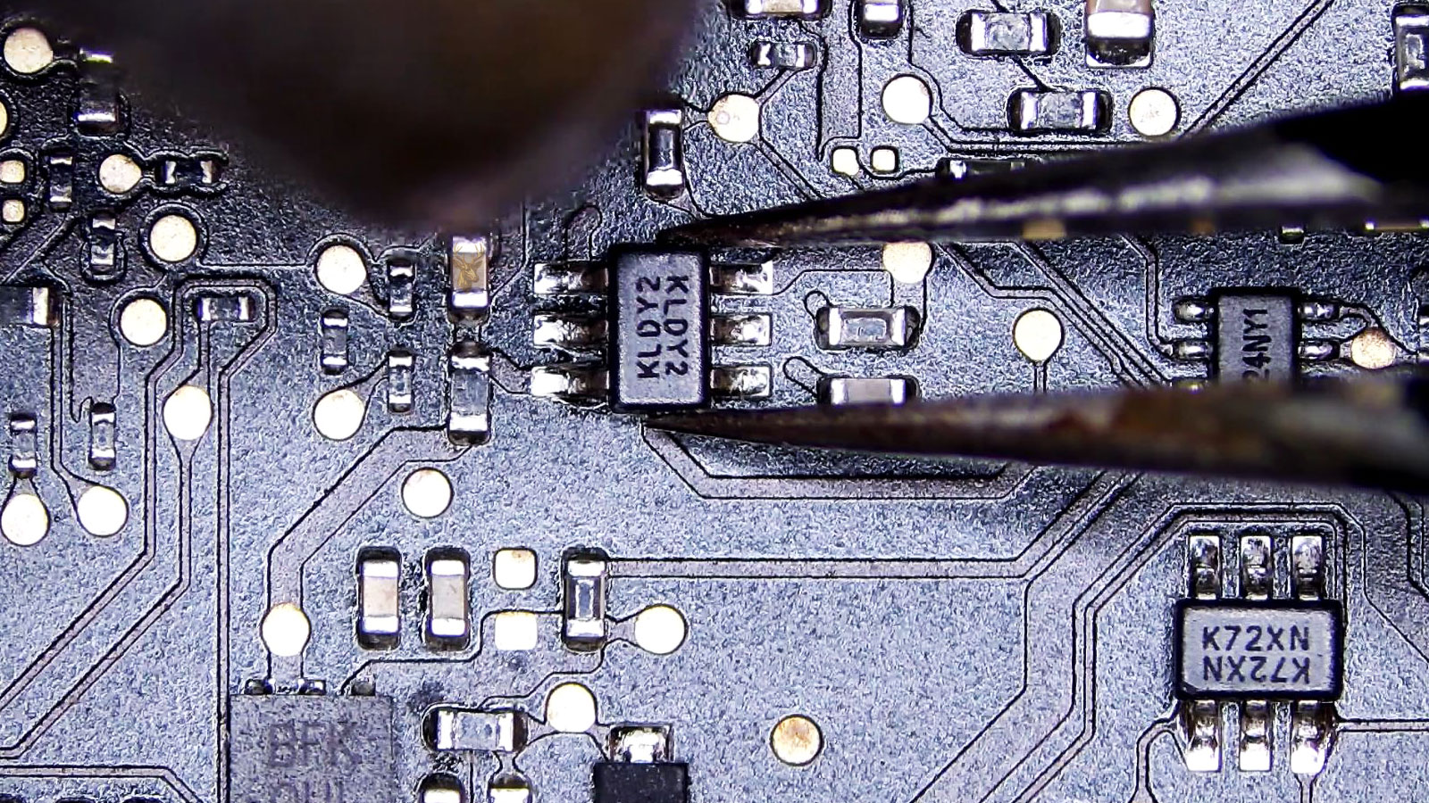 Computer circuit board with the KLDY2 IC held by tweezers while hot air is applied from above.