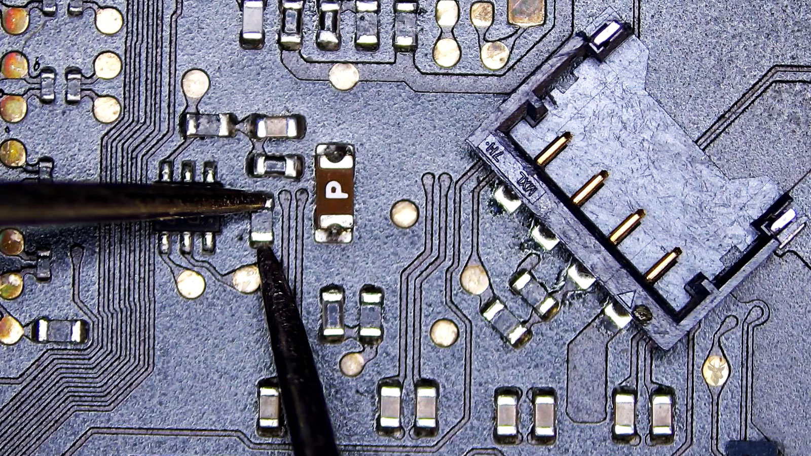 Close-up of a computer circuit board with a four-pin plastic connector, power fuse, and a small black resistor being measured with a multimeter.