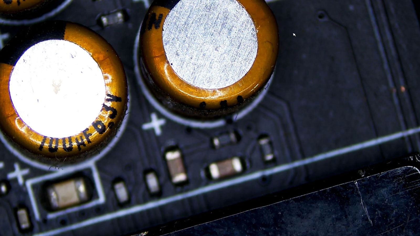 Close-up of a computer circuit board with three 100UF 6.3V capacitors, tiny SMD components, and a plus sign marking on the board.