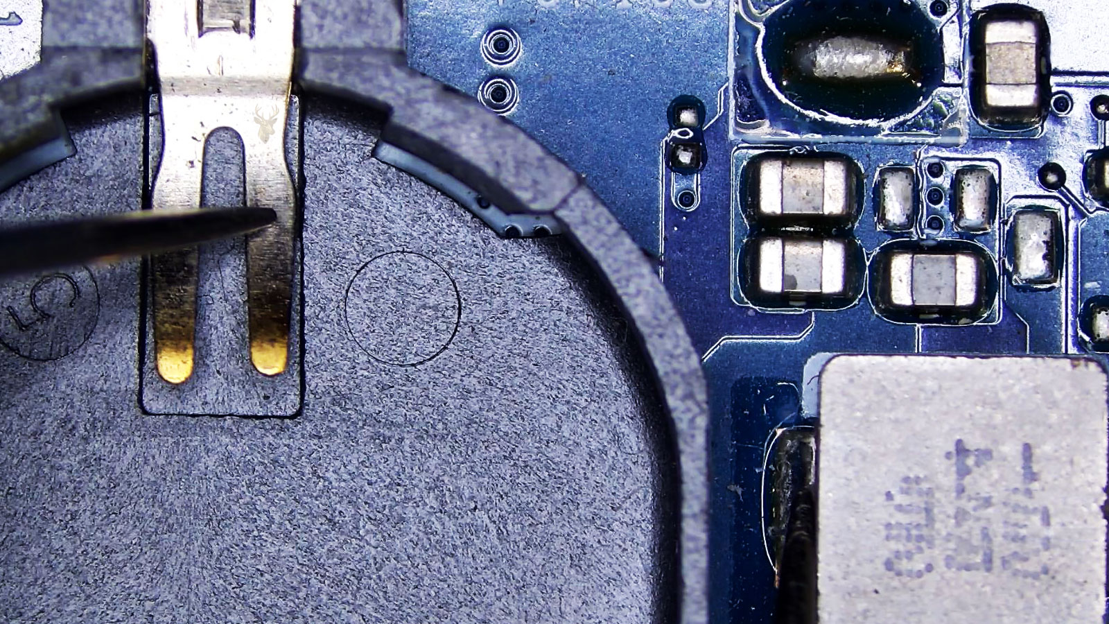 CMOS battery holder on a computer circuit board being tested with multimeter leads near capacitors, coils, and surrounding components.