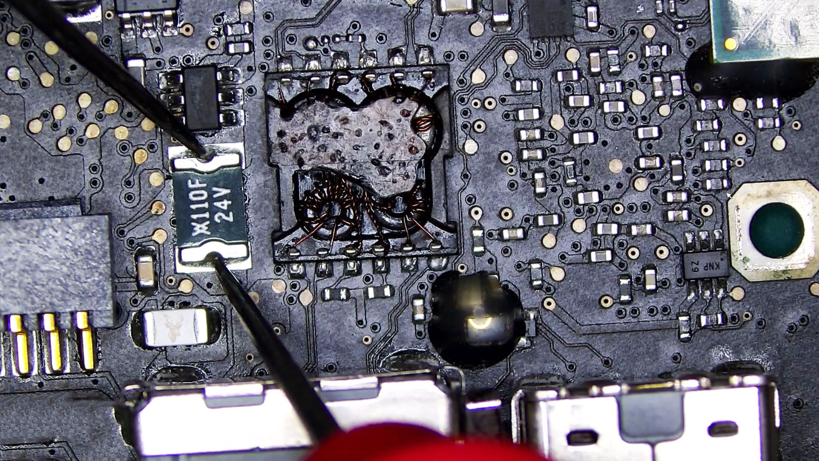 Multimeter leads testing a fuse on a computer circuit board during hardware diagnostics.