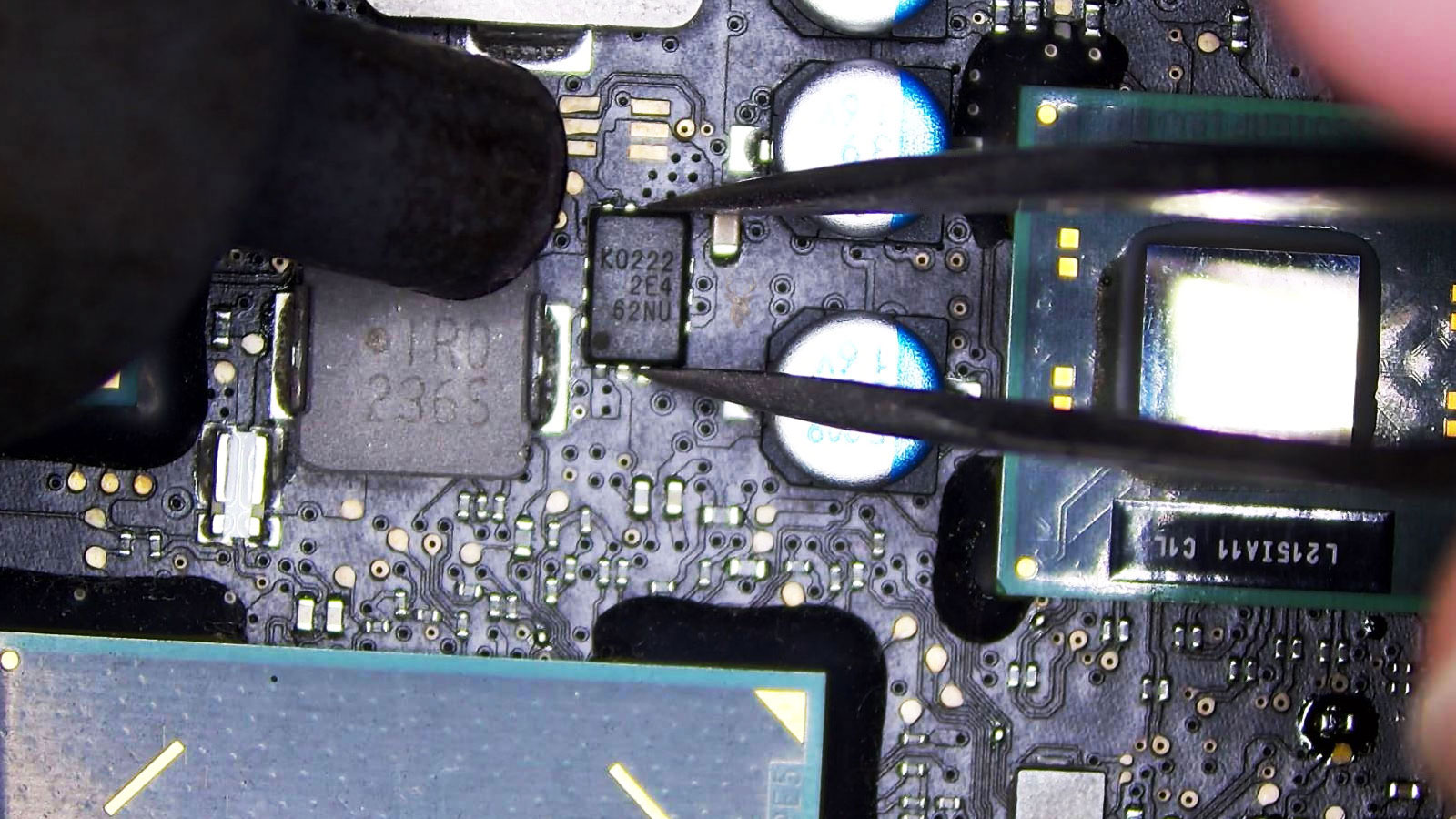 IC chip being removed from a computer circuit board with tweezers during board-level repair.