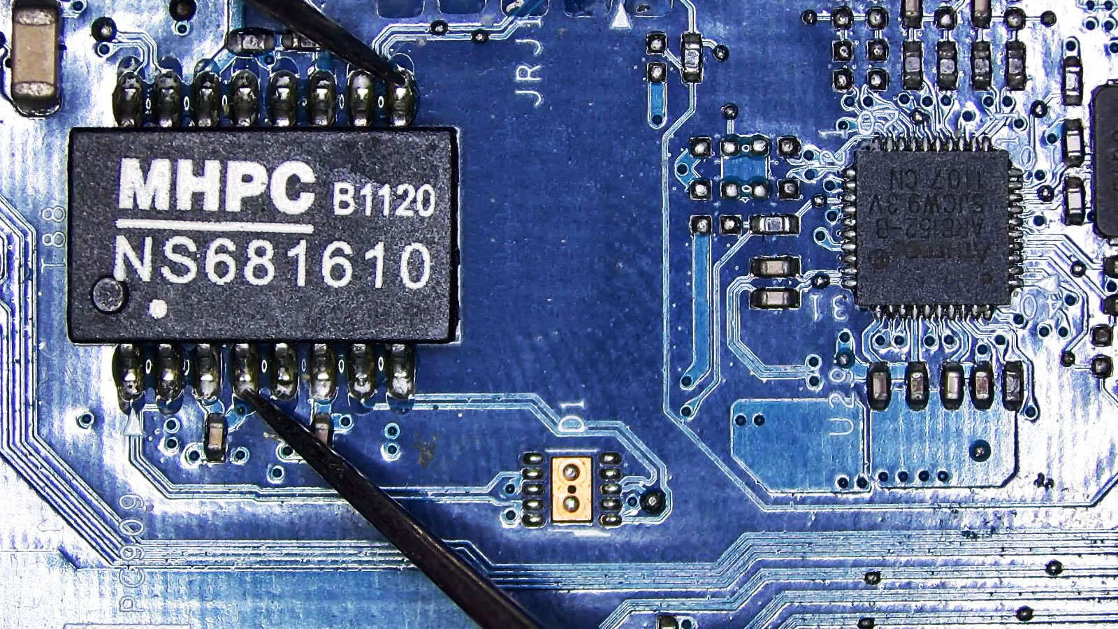 Multimeter probes testing the legs of an MHPCB1120 IC on a computer circuit board.