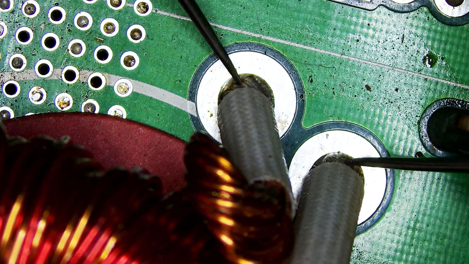 Multimeter leads testing a motherboard coil during computer hardware diagnostics.