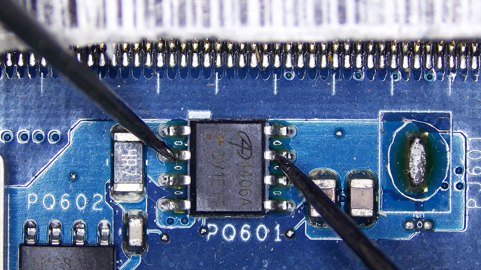 Close-up of a computer motherboard showing memory RAM slots, circuit traces, MOSFETs, transistors, capacitors, and other electronic components.