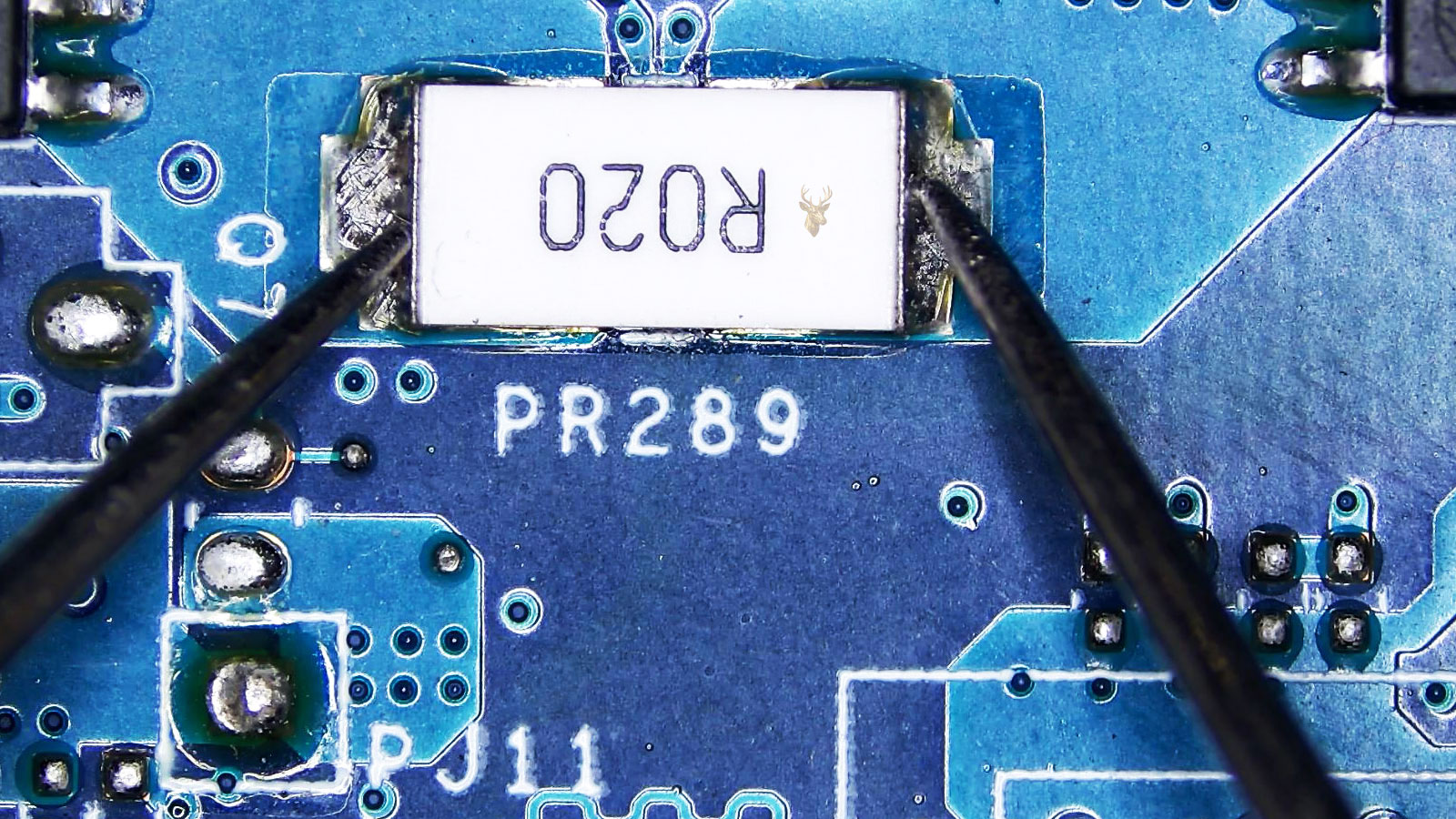 Multimeter leads testing both ends of an R020 power resistor on a computer circuit board.