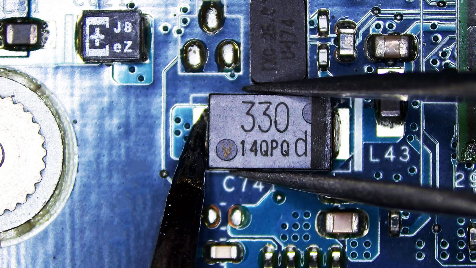 Tweezers holding a 330 capacitor while a soldering iron heats one terminal on a computer circuit board.