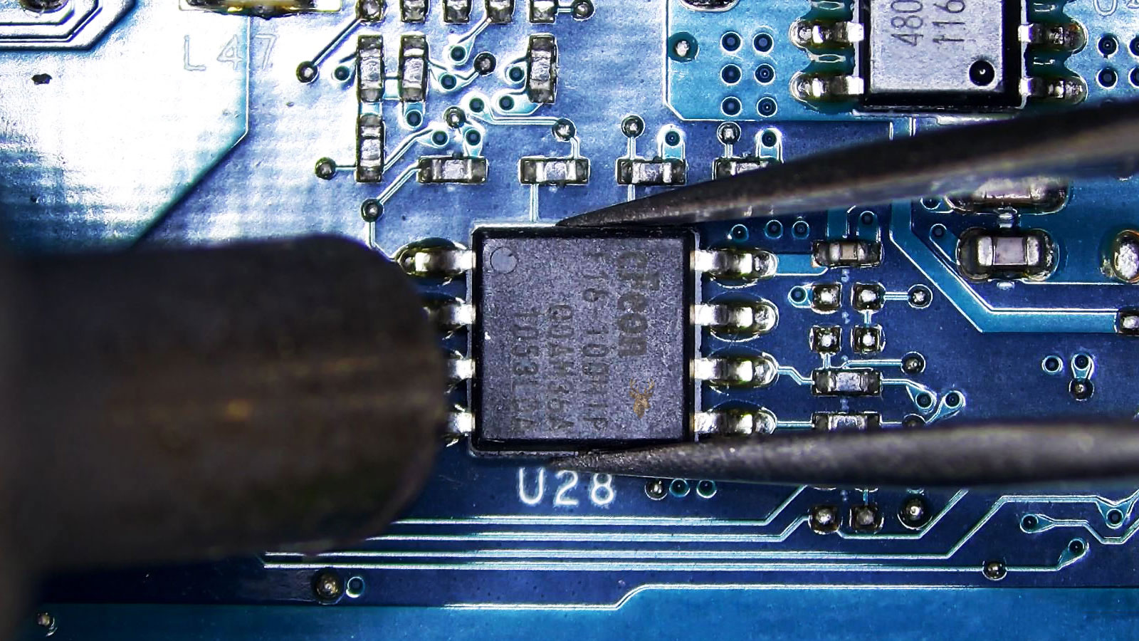 Tweezers holding the U28 eight-pin IC chip while a hot air rework nozzle heats it on a computer circuit board.