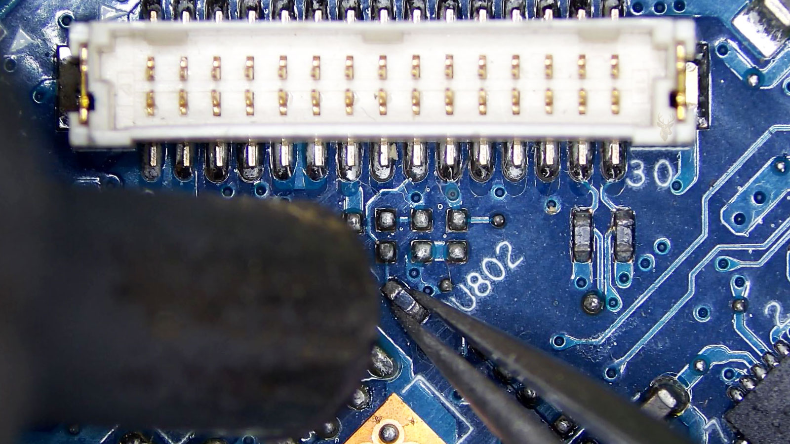 Tweezers holding the U802 component next to a board connector during computer circuit board repair.