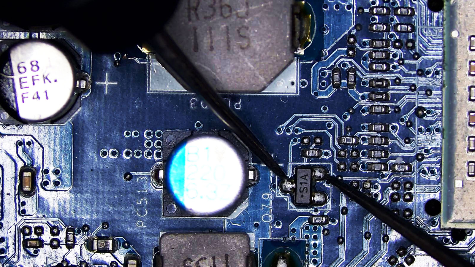 Multimeter leads testing an S1A transistor on a computer circuit board.