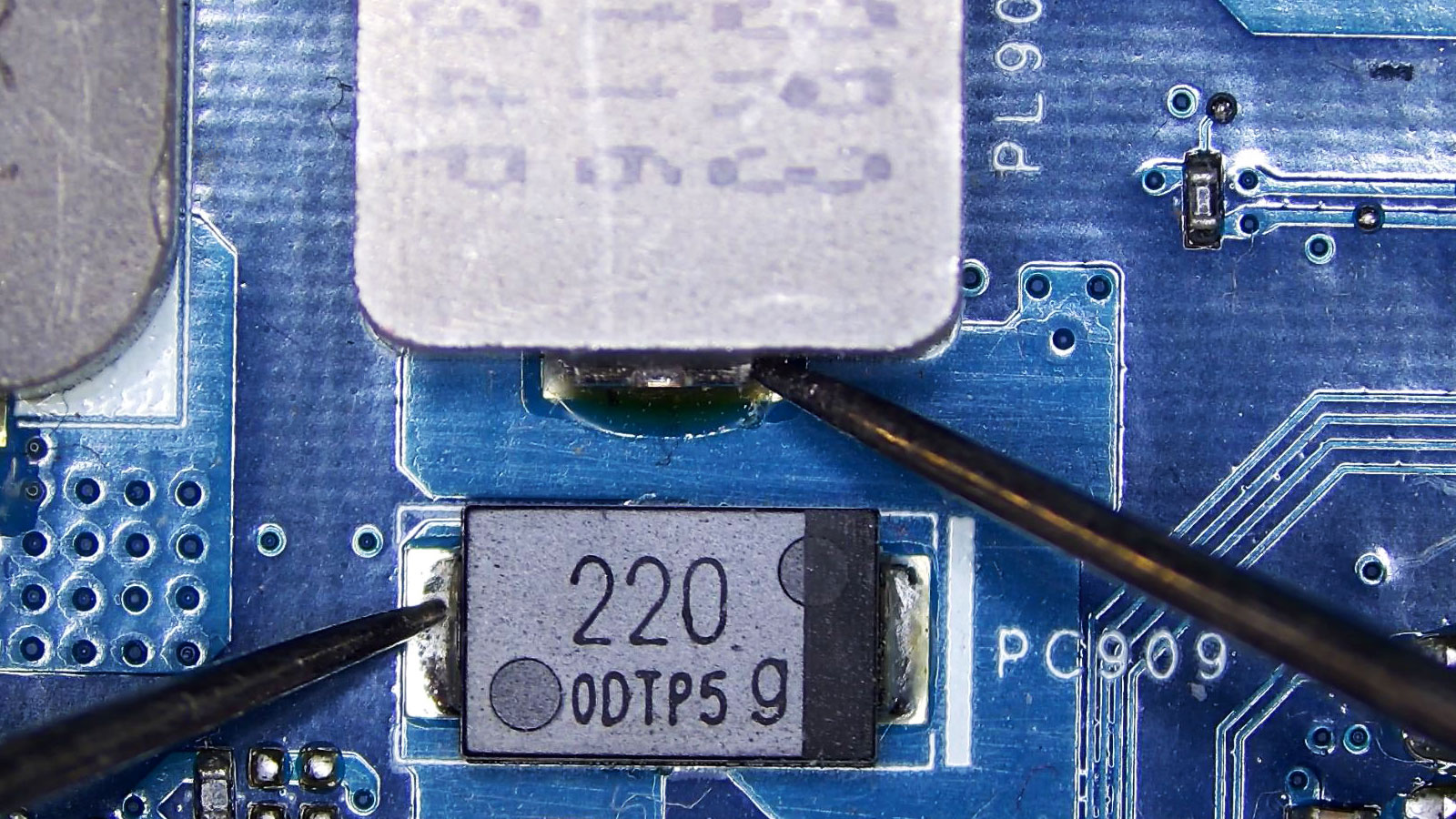 Multimeter probes testing continuity between a 220 capacitor and a power coil on a computer circuit board.