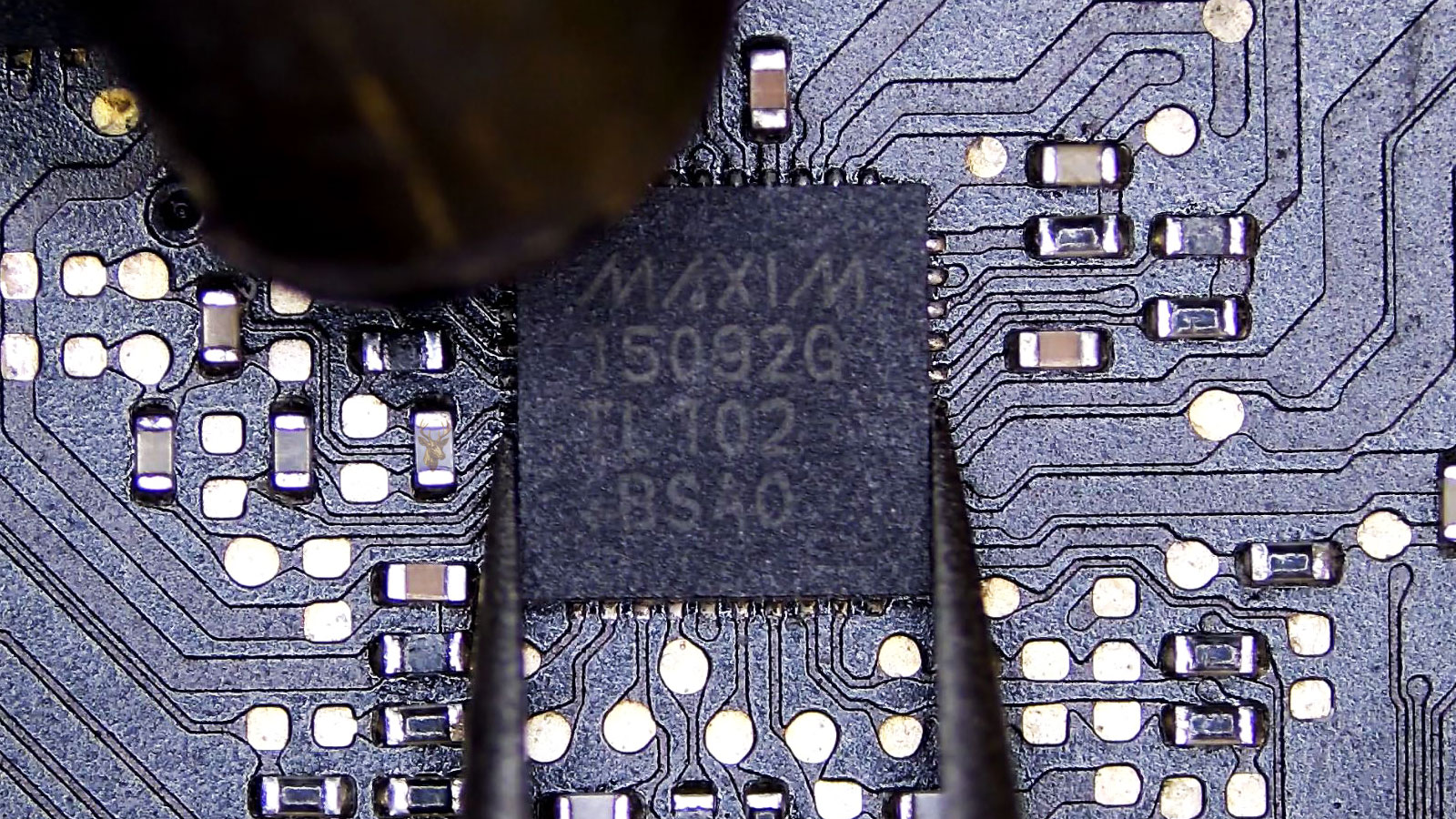 Tweezers holding the 15092G Maxim IC while a hot air gun nozzle blows air on top of it.