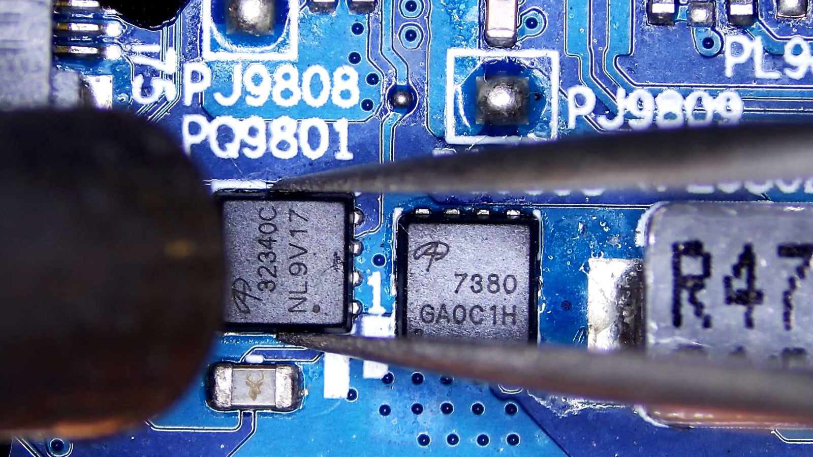 Close-up of two MOSFETs on a circuit board, with tweezers holding the A32340C component while a hot air gun points at it.