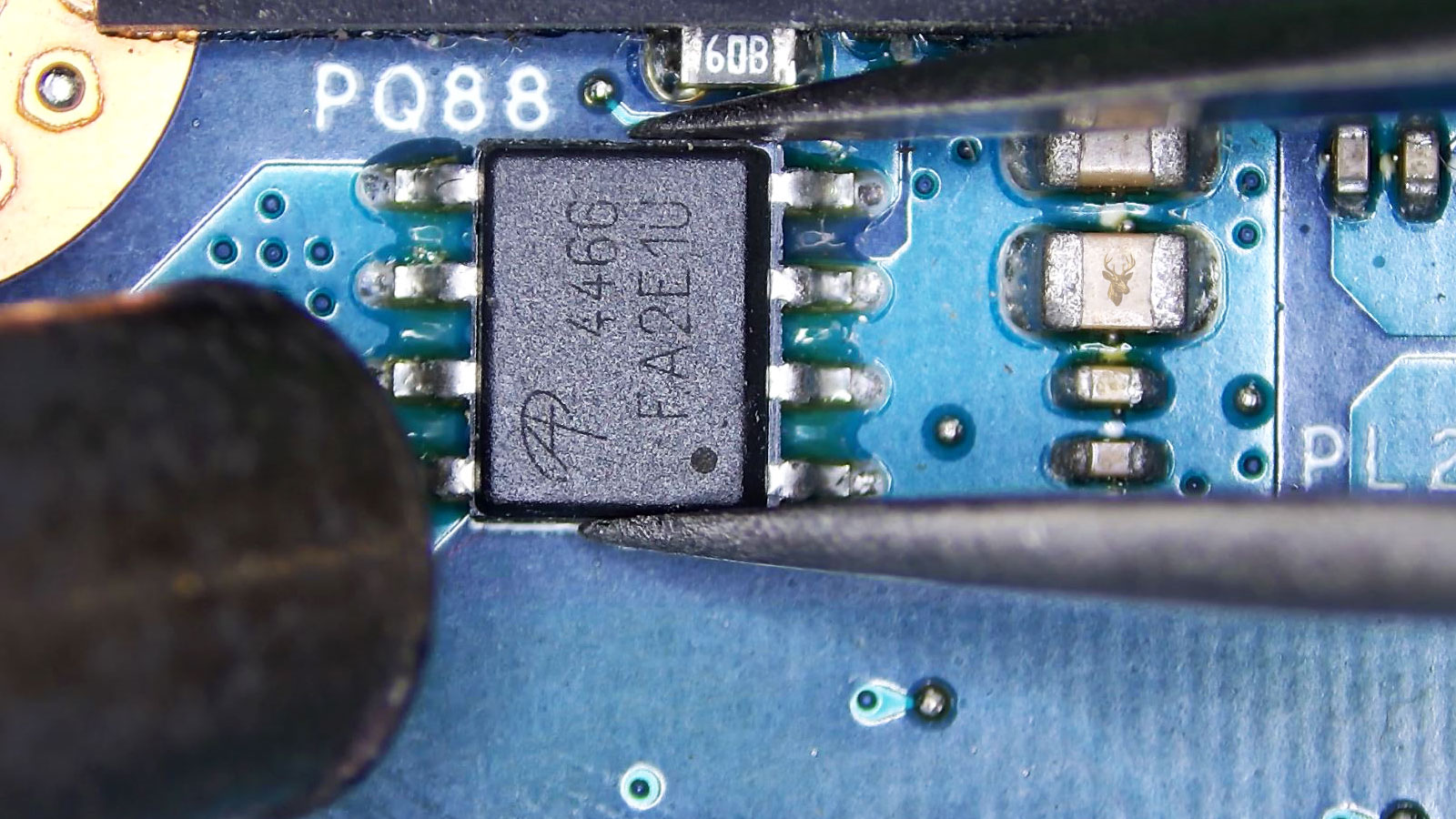 A4466 MOSFET held by tweezers while a hot air station nozzle points at it near surrounding capacitors and resistors.