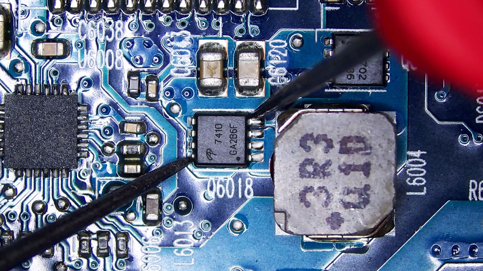 A7410 MOSFET being measured between gate and drain in a component-filled computer circuit section with capacitors, resistors, IC chips, power chips, MOSFETs, and coils.