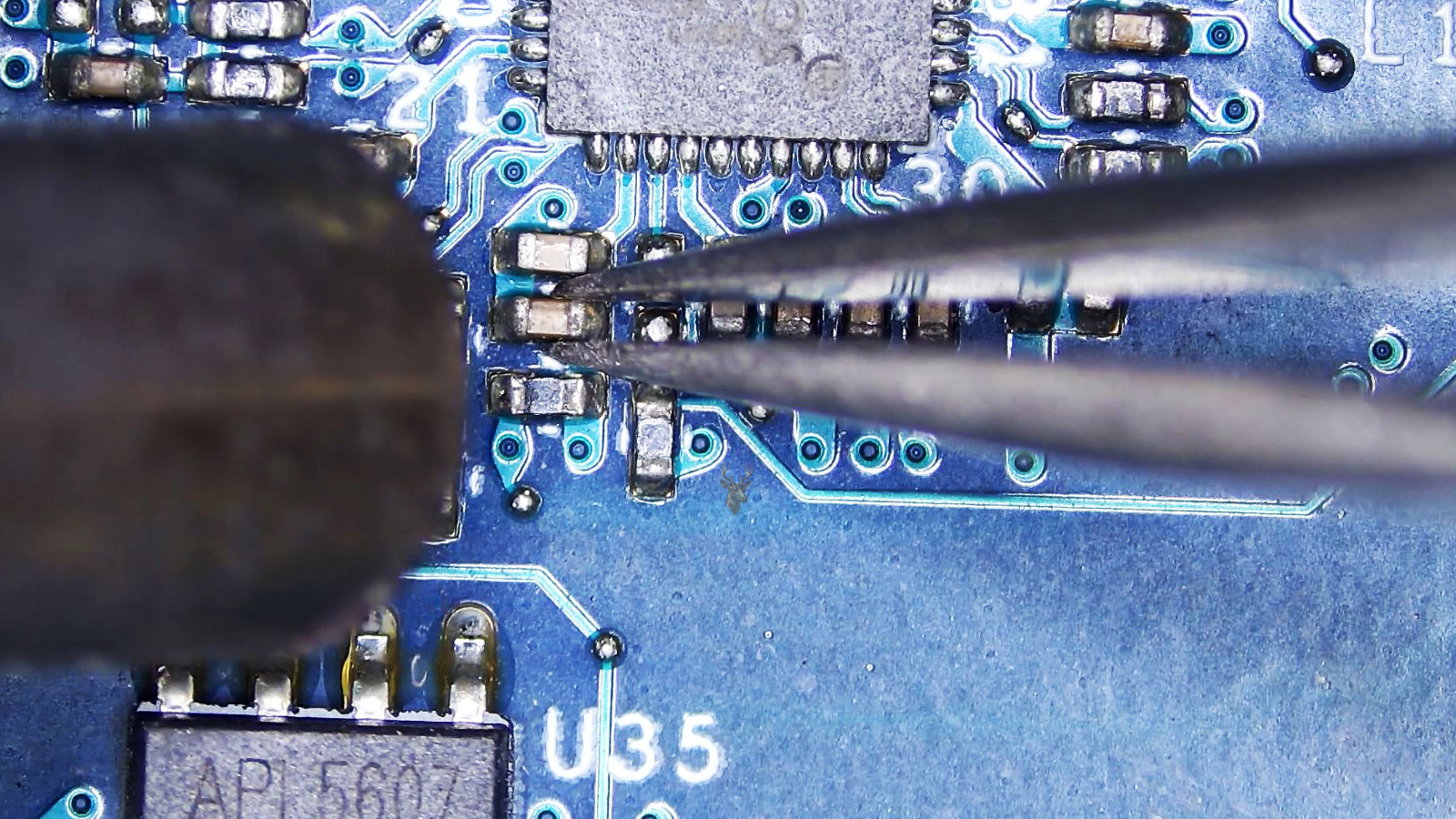 Abnormal-looking SMD capacitor held by tweezers while a hot air station points at it near an IC chip, MOSFET, resistors, and capacitors.