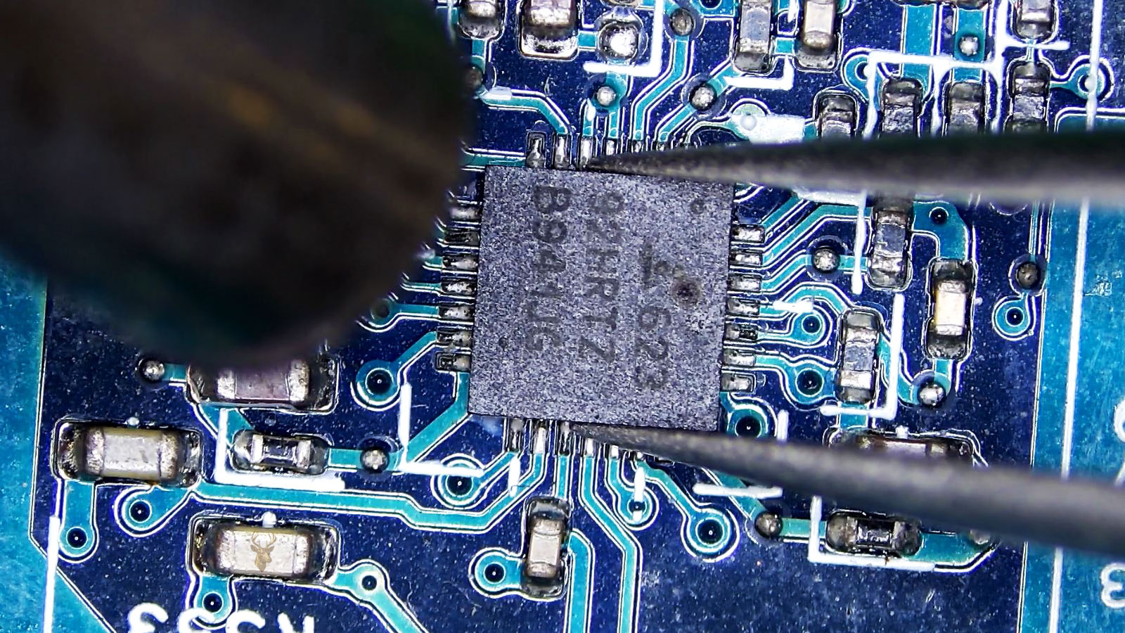 Tweezers holding the burned 623928RTZ B941JG IC while a hot air gun nozzle points toward it.