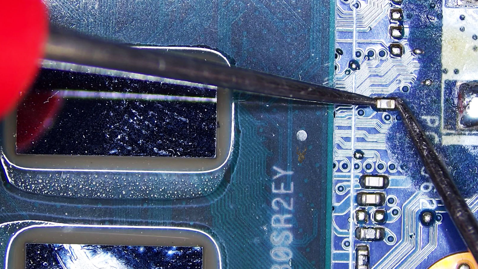Close-up of a computer circuit board near the CPU and GPU area with a capacitor being measured.