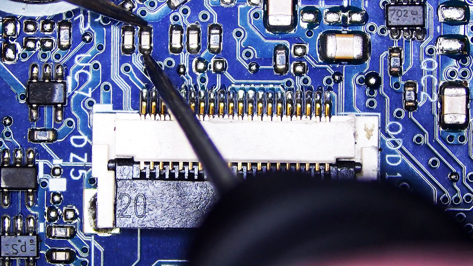 Capacitor being measured next to a 20-pin connector on a computer circuit board with surrounding transistors, resistors, capacitors, and ICs.