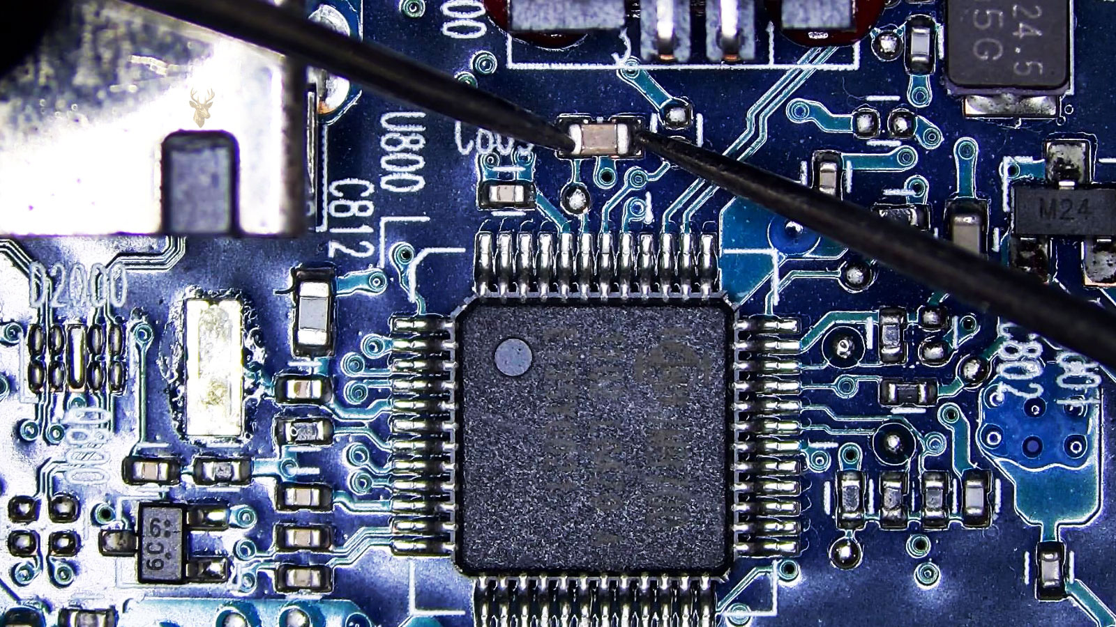Capacitor being measured next to a 48-pin IC chip on a complex circuit section with a transistor, capacitors, connector, USB-style port, and HDMI-style port.