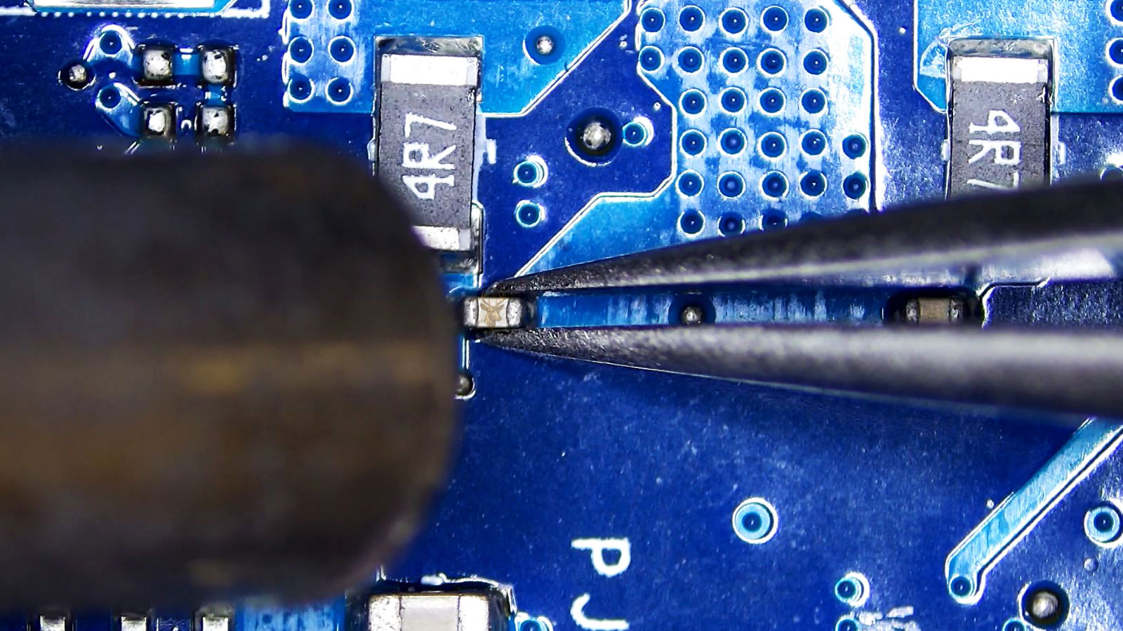 Tweezers holding a capacitor beside one 4R7 resistor while a hot air gun nozzle points toward it.