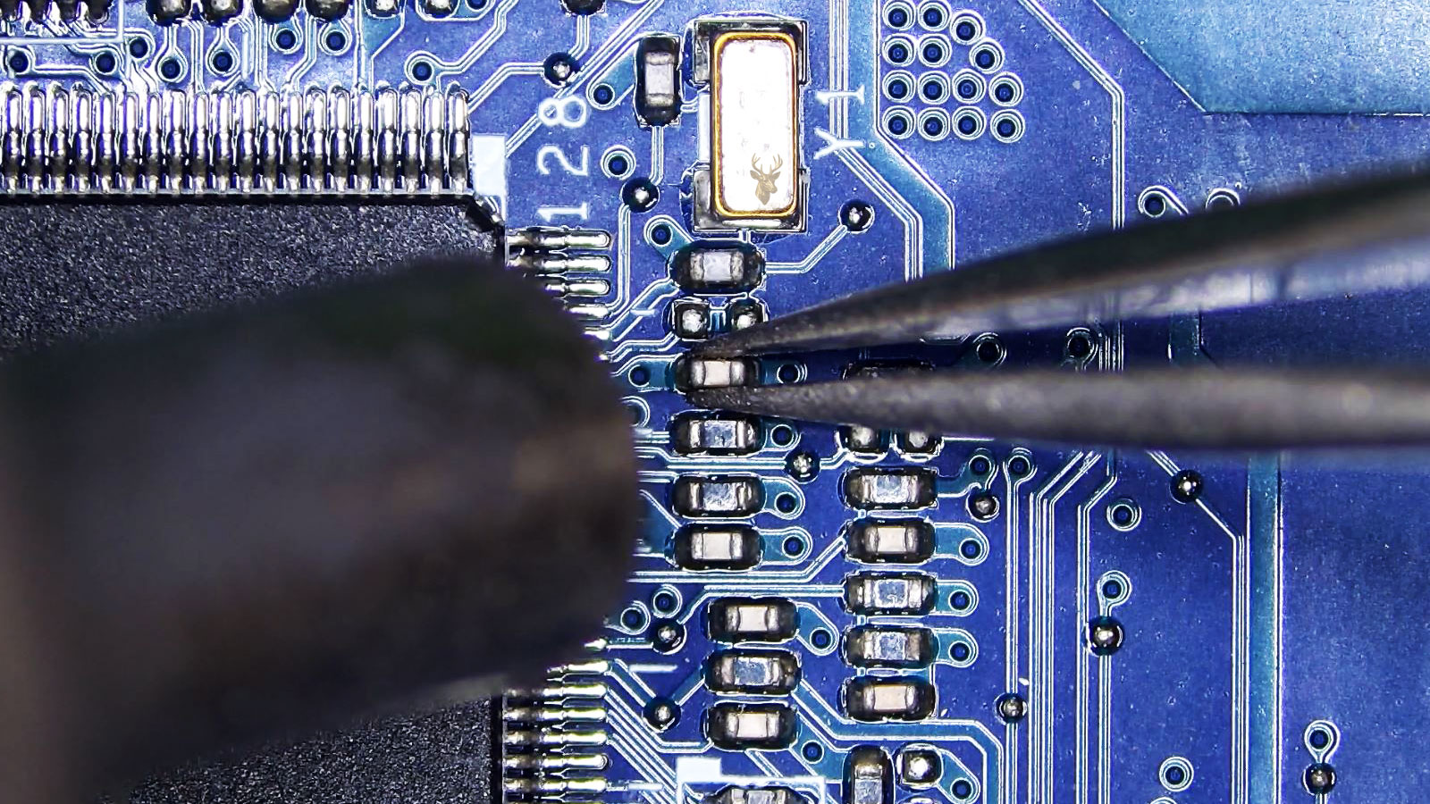 Small capacitor beside the ENE Super I/O chip held by tweezers while a hot air station points at it near surrounding board components.