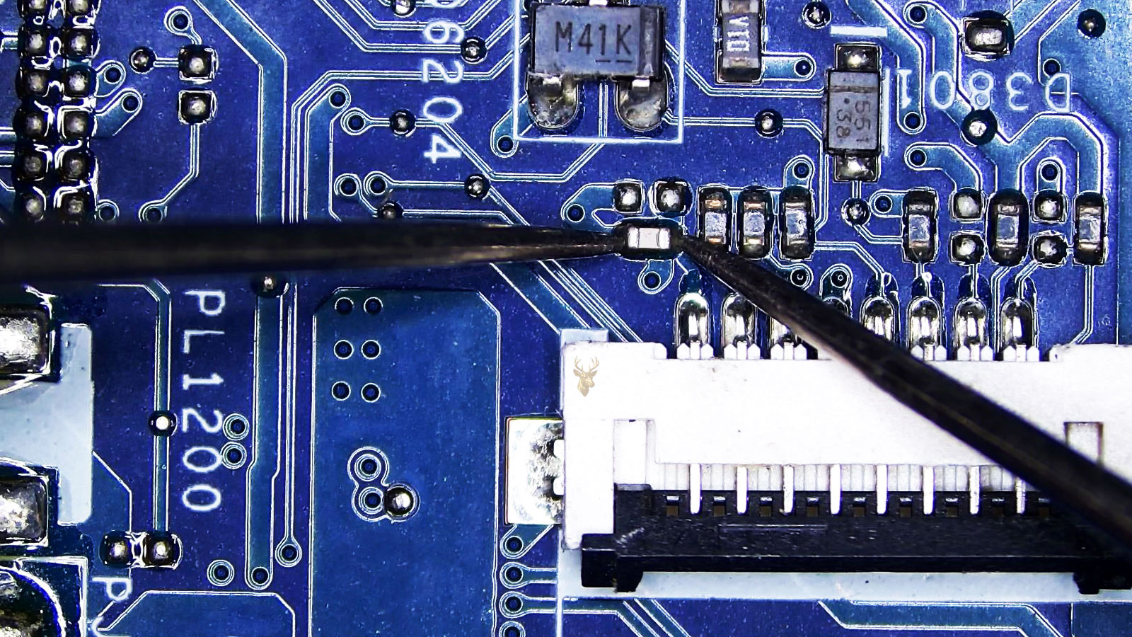 Capacitor being measured beside a large 8-pin plastic ribbon cable connector on a computer circuit board with nearby resistors, diodes, transistors, and capacitors.