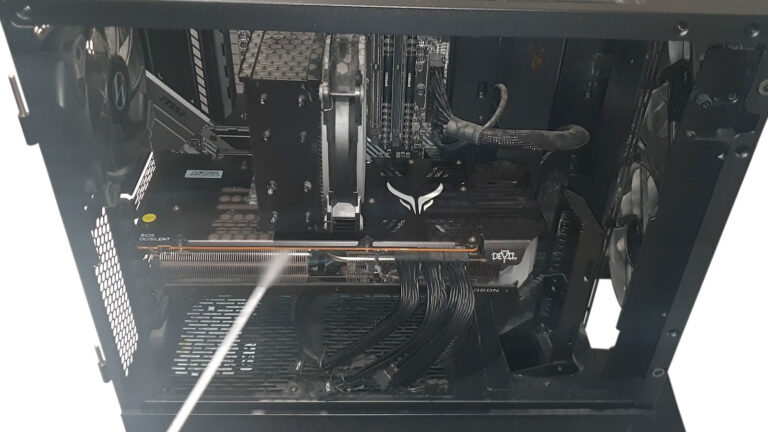 Open desktop computer being cleaned with a can of compressed air directed toward the graphics card and internal components.