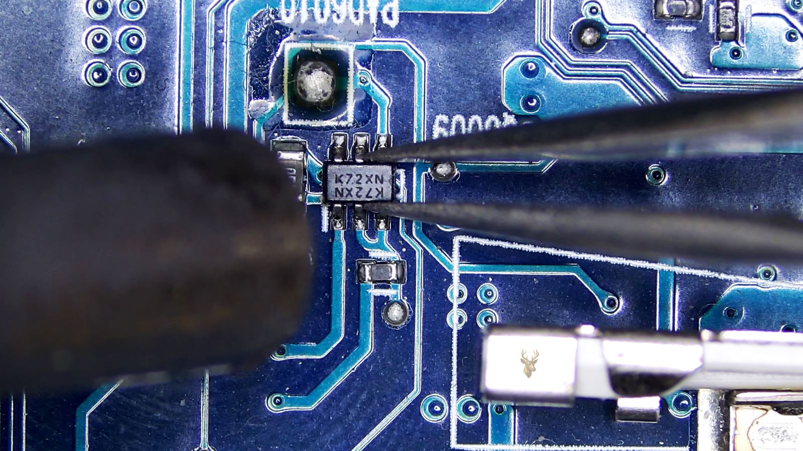 K72XN tiny controller held by tweezers near the memory lock area while a hot air station points at it.