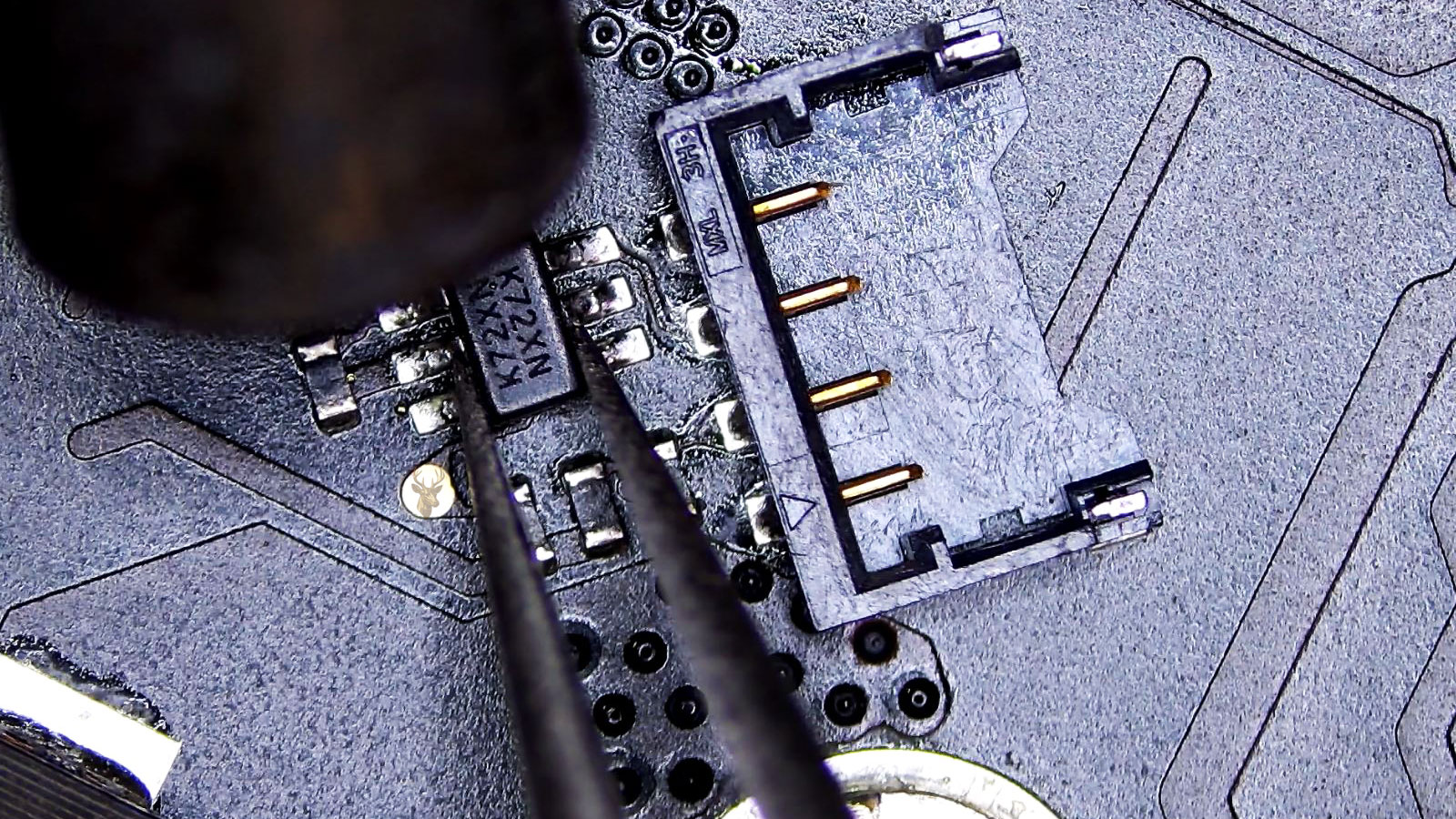 Tweezers holding the K72XN IC while a hot air gun nozzle points toward it.