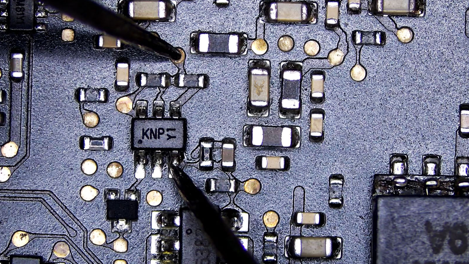 Multimeter measuring between a KMPY1 transistor leg and a round test pad on the circuit.