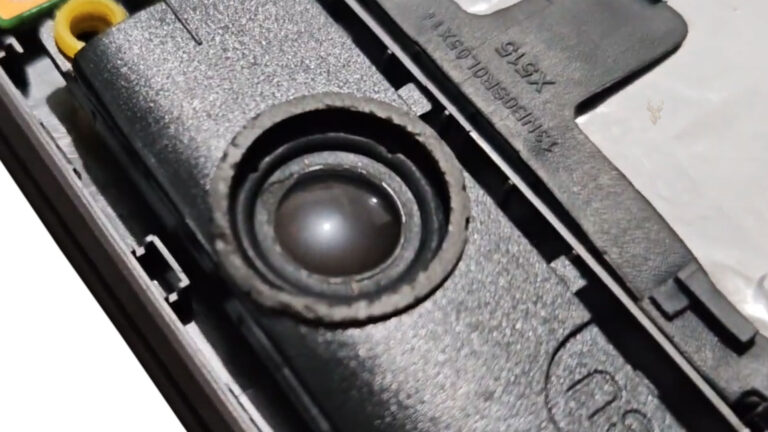 Damaged laptop speaker with a cracked and loosened center, representing audio that crackles, distorts, or stops working at certain volumes.