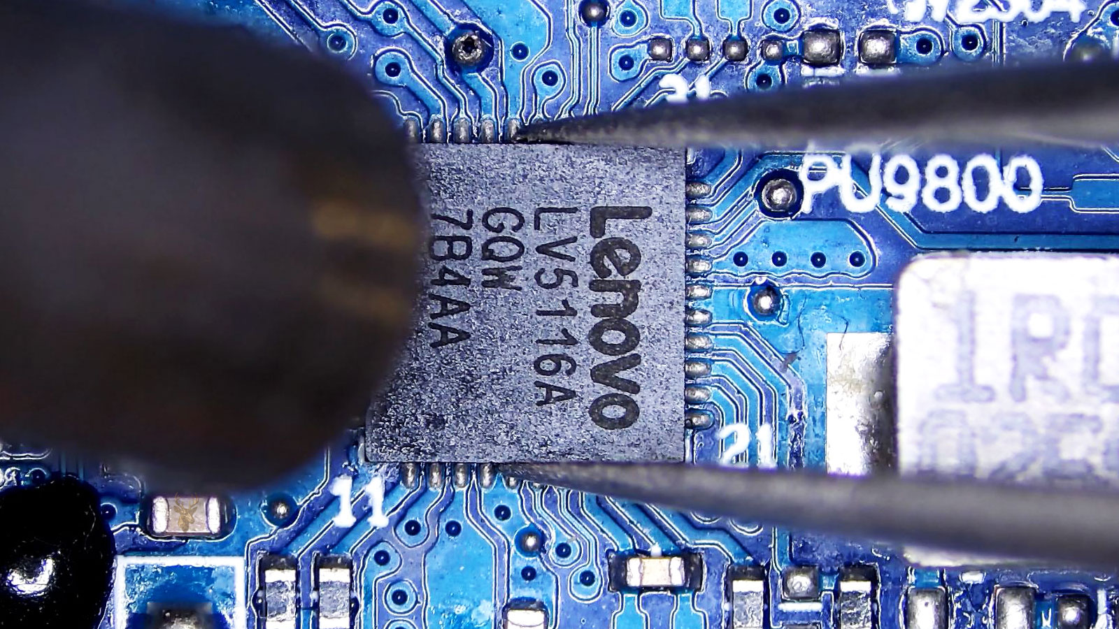 Lenovo LV5116A power IC held by tweezers while a hot air station points at it near a coil and surrounding components.