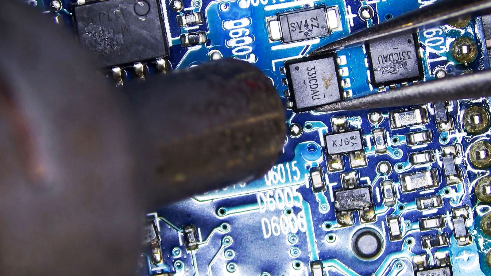 Tweezers holding a suspected 331CDAU MOSFET while a hot air station nozzle points at the component on a densely populated circuit board.