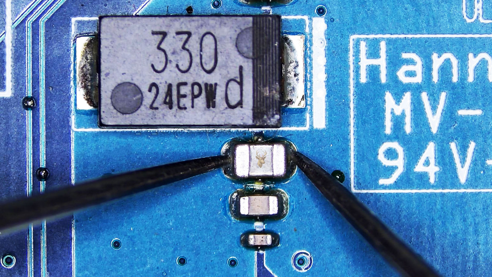 Multimeter probe measuring one capacitor in a circuit area with several nearby capacitors and a large 330-marked component.