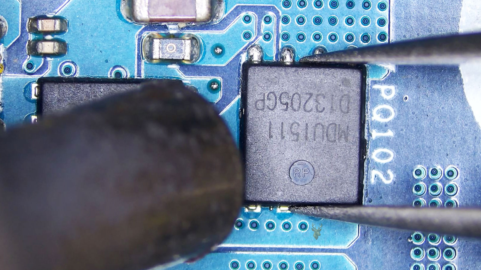 PQ102 MOSFET held by tweezers while a hot air station nozzle points at it near another MOSFET, capacitors, resistors, and small caps.