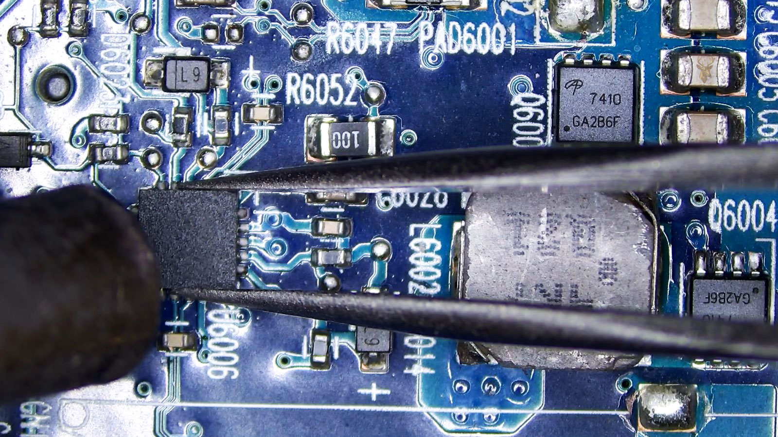 Power controller held by tweezers under a hot air station nozzle, surrounded by transistors, diodes, MOSFETs, coils, and power components.