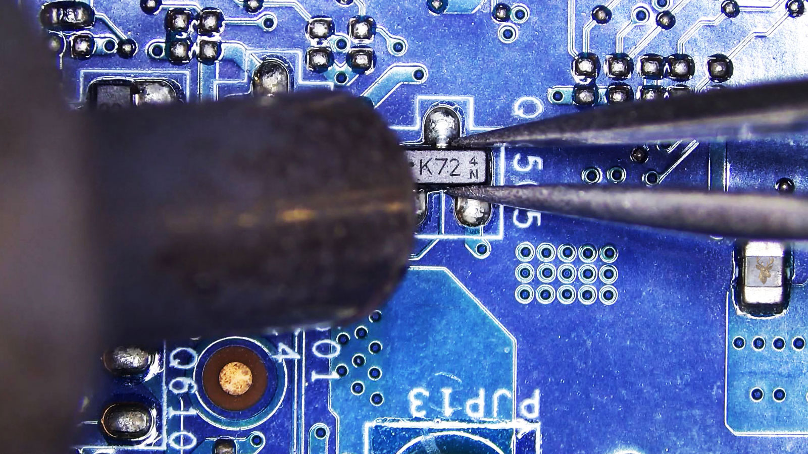 Tweezers holding the Q2505 transistor while a hot air station nozzle points at it among nearby transistors and a small controller.
