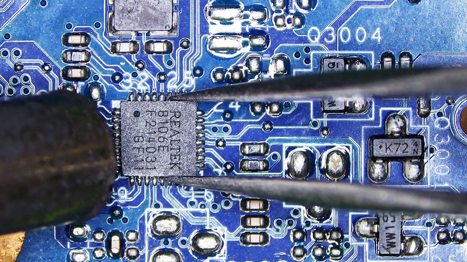 Realtek 8106E chip held by tweezers while a hot air station points at it among capacitors, resistors, transistors, coils, and fuses.