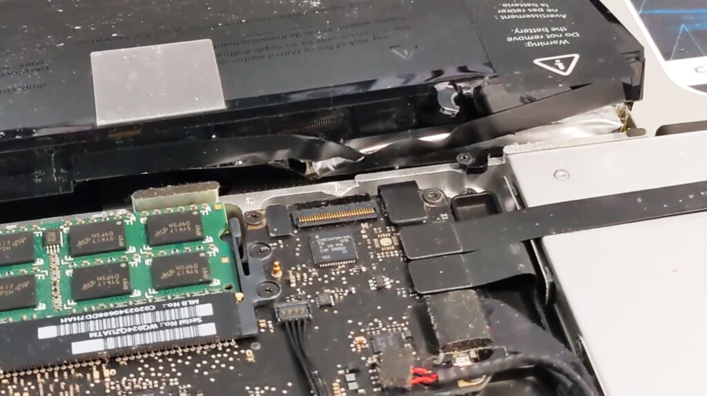 Severely swollen laptop battery with a cracked casing and damaged mounting area caused by internal expansion.