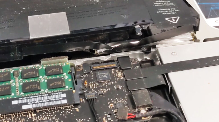 Severely swollen laptop battery with a cracked casing and damaged mounting area caused by internal expansion.