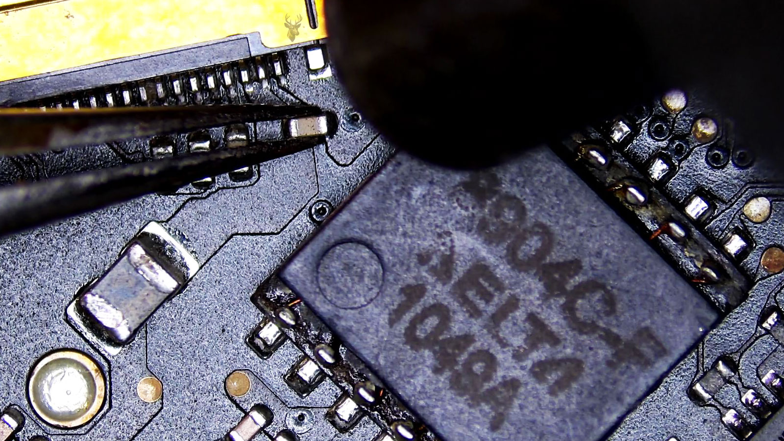 Tiny SMD capacitor held by tweezers between the yellow LCD connector and Delta 1049A IC with a hot air nozzle aimed at it.