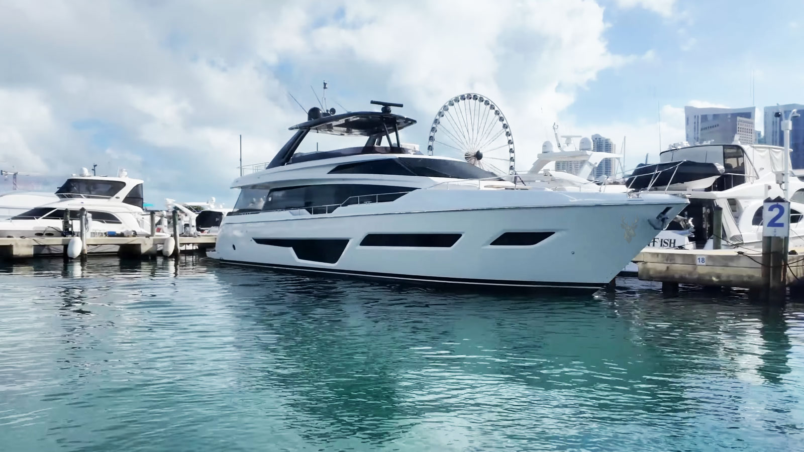 Large white and blue luxury yacht surrounded by boats in a scenic bay.