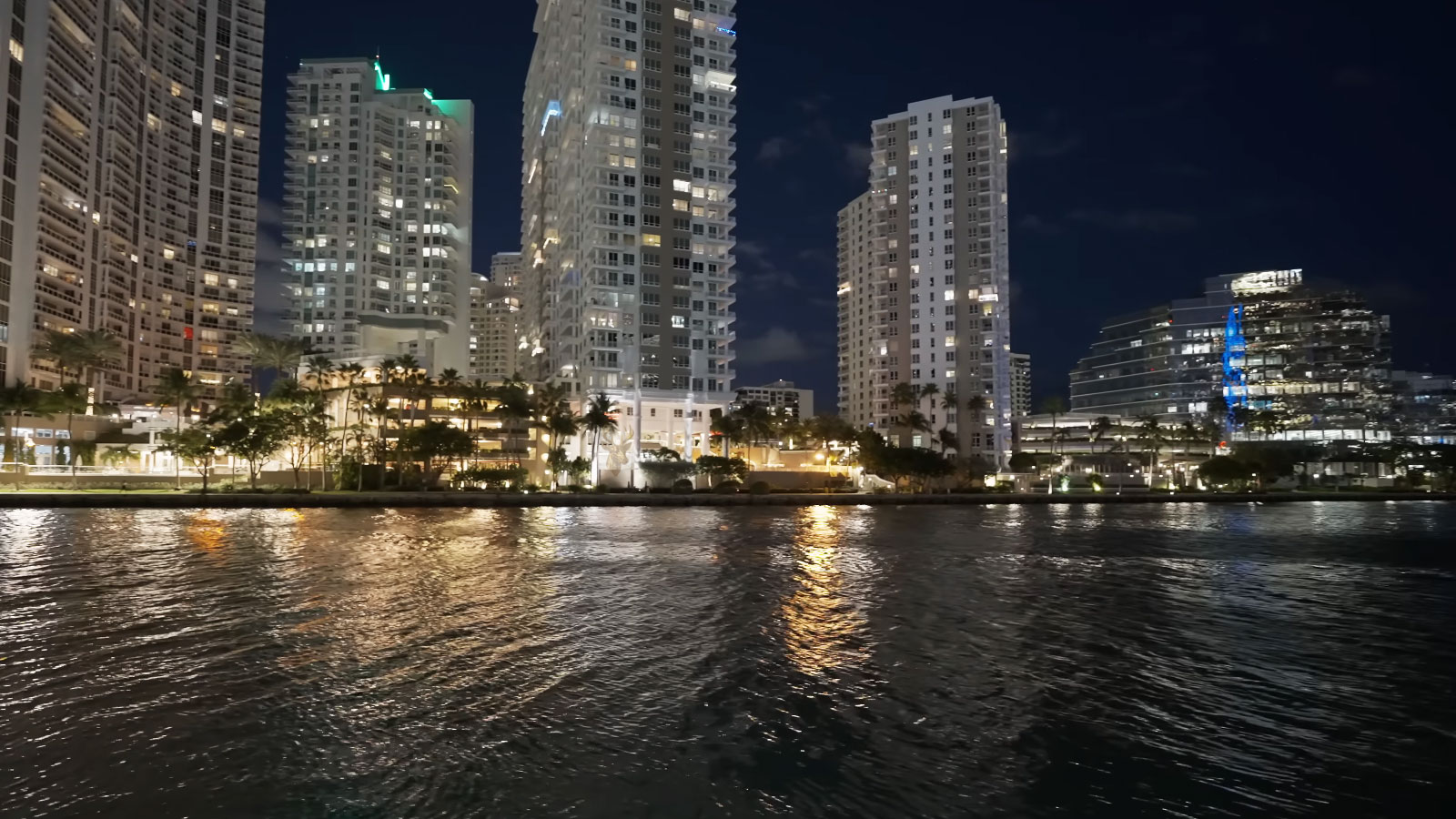 Nighttime city skyline with illuminated high-rise buildings along a waterfront.